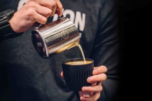 Person pouring latte art into a black huskee cup